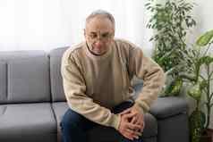 男人。膝盖联合疼痛沙发疼痛上了年纪的健康护理上了年纪的护理上了年纪的男人。膝盖疼痛坐着祖父膝盖疼痛