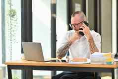 英俊的成人男人。员工白色衬衫眼镜电话谈话坐着桌子上现代办公室