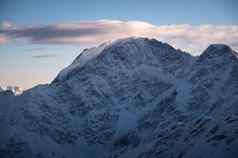 美丽的山山峰雪冬天日落色彩斑斓的景观高雪悬崖雾蓝色的天空云冷晚上