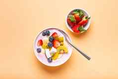 健康的早餐甜点酸奶碗新鲜的香蕉草莓蓝莓可可猕猴桃前视图最小的柔和的纸背景勺子