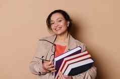 中年女人老师高学校机构微笑相机携带堆栈书米色背景