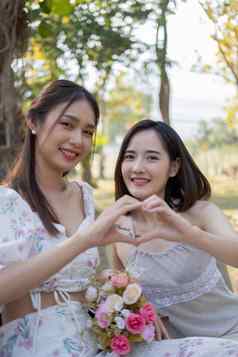亚洲女人朋友野餐说话幸福的迷人的亚洲女人使心手标志朋友野餐公园