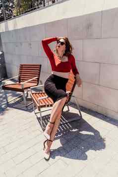 肖像女人街有吸引力的女人眼镜红色的上衣黑色的裙子坐着板凳上