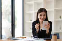亚洲女商人智能手机会计工作移动PC图金融报告办公室