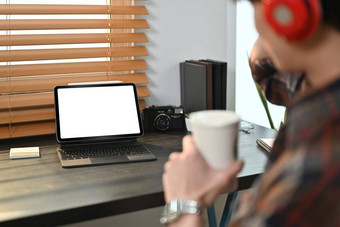 裁剪图像赶时髦的人男人。喝咖啡坐着前面数字平板电脑空白屏幕黑色的木桌子上