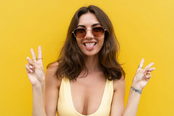 年轻的美丽的女人无忧无虑的女人摆姿势街黄色的墙积极的模型在户外太阳镜快乐快乐的显示标志