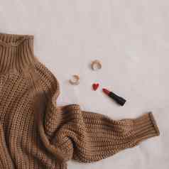 开销视图女人的休闲装温暖的针织毛衣红色的口红耳环米色背景床上平躺前视图