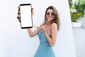肖像美丽的女人绿色夏天衣服白色背景自然日光指出空白色大屏幕智能手机空间广告