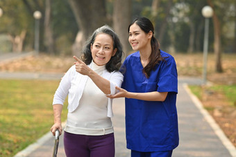 微笑高级女人会说话的有爱心的年轻的护士走户外援助康复概念