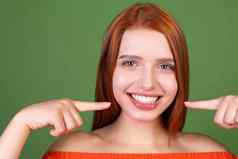 年轻的红色的头发女人休闲橙色上衣绿色背景点手指白色牙齿完美的微笑