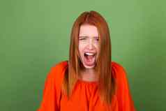 年轻的红色的头发女人休闲橙色上衣绿色背景伤心愤怒的失望尖叫