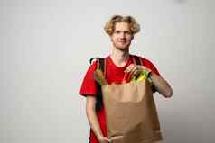 交付概念英俊的年轻的交付男人。红色的统一的携带包盒子杂货店食物喝商店市场白色工作室背景