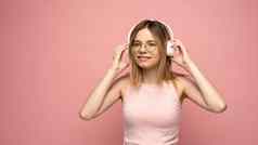 美丽的年轻的金发女郎女人耳机移动设备听音乐微笑跳舞孤立的粉红色的背景