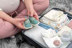 怀孕了女人持有婴儿鞋子包装孕妇医院袋妈妈。怀孕