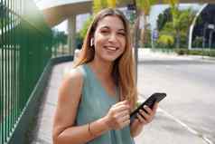 巴西女人微笑相机智能手机社会媒体城市耳机在户外快乐拉丁女学生微笑互联网连接技术手机