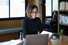 肖像十几岁的亚洲女人穿眼镜电脑移动PC耳机移动PC研究在线视频会议木图书馆表格