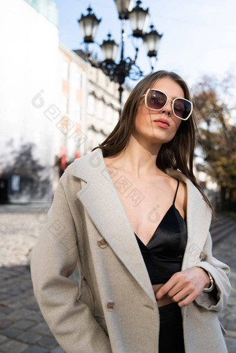 迷人的浅黑肤色的女人摆姿势街春天穿时尚的米色外套前剃须刀太阳镜