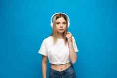 快乐的年轻的金发女郎女人女孩白色衣服听音乐耳机移动电话孤立的蓝色的背景工作室人生活方式概念