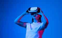 元宇宙概念年轻的浅黑肤色的女人女人白色t恤穿耳机玩视频游戏互动虚拟现实霓虹灯光