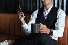 肖像不错的谨慎的亚洲男人。坐着沙发智能手机喝咖啡