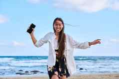 快乐的女人耳机智能手机听音乐跳舞海滩