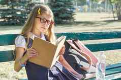 户外肖像漂亮的女孩学校统一的眼镜背包瓶水阅读书
