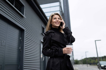 年轻的女人投资者会说话的电话背景业务建筑持有杯咖啡手