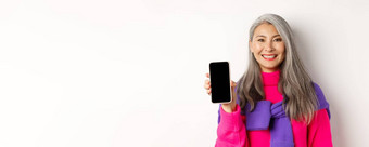 在线购物特写镜头微笑亚洲祖母显示空白智能手机屏幕推荐促销活动站白色背景