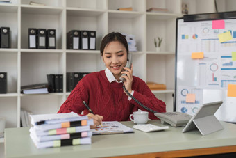 美丽的亚洲女人会说话的电话有创意的<strong>办公室</strong>快乐微笑女商人回答电话<strong>办公室</strong>桌子上<strong>休闲</strong>业务女人坐着桌子上使电话调用采取请注意