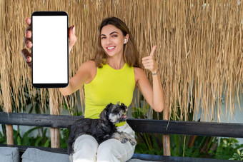 肖像快乐的女人站户外智能手机耳机微型雪纳瑞犬小狗狗持有电话白色空大屏幕快乐微笑