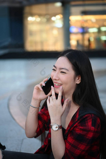 快乐亚洲女人坐着城市街晚上会说话的移动电话