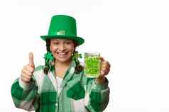 微笑女人快乐的情绪拇指持有杯子绿色啤酒庆祝帕特里克的一天酒吧聚会，派对3月