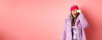 购物时尚概念美丽的亚洲中年女人显示塑料信贷卡脸兴奋相机站粉红色的背景