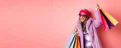 时髦的很酷的亚洲高级女人时尚衣服跳舞购物销售持有商店纸袋有趣的粉红色的背景