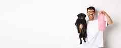 图像快乐男人。宠物老板持有可爱的黑色的哈巴狗狗粪便袋站白色背景