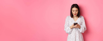 紧张有关亚洲女人阅读消息智能手机担心站衣服粉红色的背景