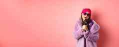时尚概念时尚的高级亚洲女人唱歌卡拉ok执行阶段麦克风穿时尚的太阳镜紫色的人造皮毛外套粉红色的背景