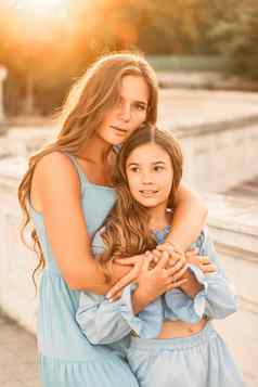 肖像妈妈。女儿蓝色的礼服流动长头发背景日落女人拥抱按女孩相机