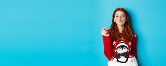冬天假期圣诞节夏娃概念可爱的红色头发的人女孩圣诞节毛衣显示心标志皱纹嘴唇吻站蓝色的背景
