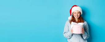 冬天假期圣诞节夏娃概念可爱的红色头发的人女孩毛衣圣诞老人他持有一年礼物相机站蓝色的背景