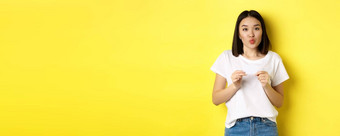 年轻的亚洲女人休闲白色t恤显示塑料信贷卡皱纹嘴唇愚蠢的购物黄色的背景