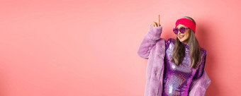 亚洲女人时尚闪闪发光的衣服紫色的人造皮毛外套跳舞迪斯科指出手指有趣的粉红色的背景