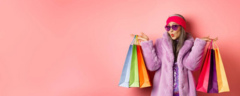 时尚的亚洲高级女人购物穿时尚的衣服太阳镜持有商店袋衣服购买粉红色的背景