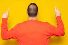 拉美裔男人。红色的运动衫指出指数手指回来相机孤立的黄色的背景