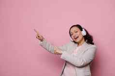 可爱的微笑多民族女人无线耳机指出食指复制空间孤立的粉红色的背景