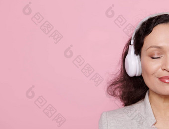 一半脸令人愉快的女人耳机享受舒缓的音乐摆姿势眼睛关闭粉红色的背景复制空间