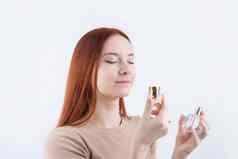 快乐年轻的女人闻香水持有玻璃瓶孤立的白色背景
