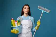 女人更清洁的围裙持有桶洗涤剂扫帚