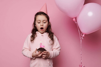可爱的孩子生日女孩吹蜡烛节日蛋糕使珍惜孤立的粉红色的背景