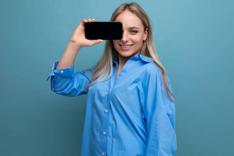 微笑非正式的金发碧眼的女孩持有智能手机空白屏幕模型网站蓝色的背景